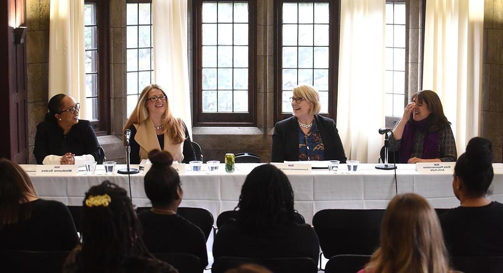 A panel of smiling and laughing women are seated at a PCWP event